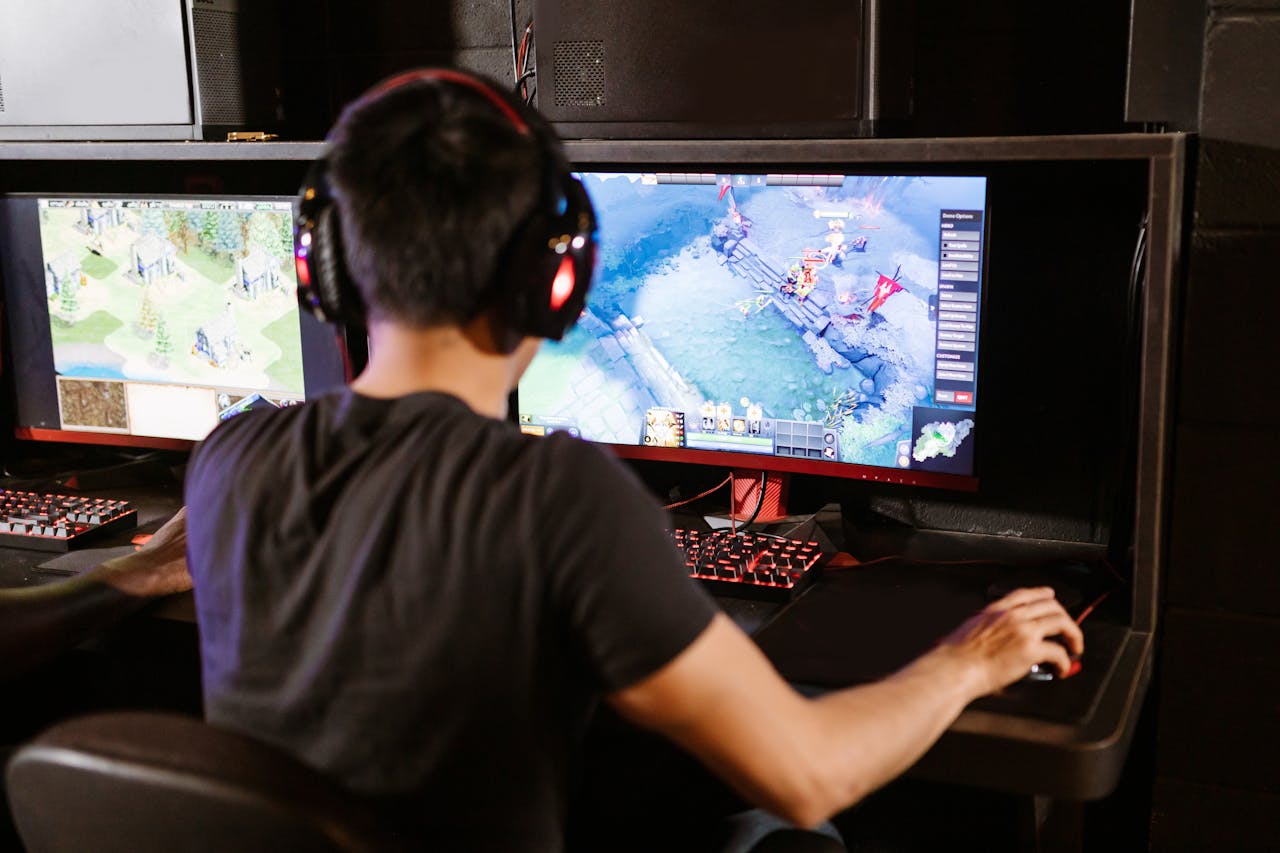 gallery-6 Adult male gamer immersed in PC gaming on dual monitors with headphones indoors.