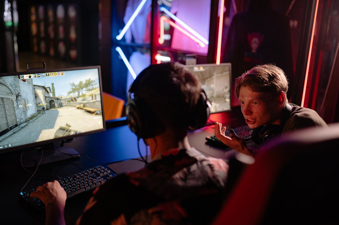services-02 Two gamers engaged in a heated video game session surrounded by neon lights and computer screens.